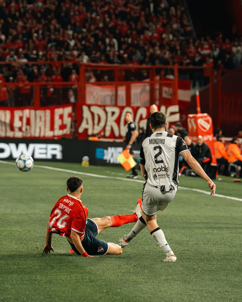Un défenseur glisse pour contrer une frappe, un soir de match devant une tribune pleine